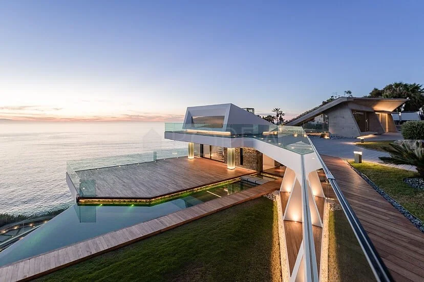 Villa con piscina desbordante frente al mar al atardecer